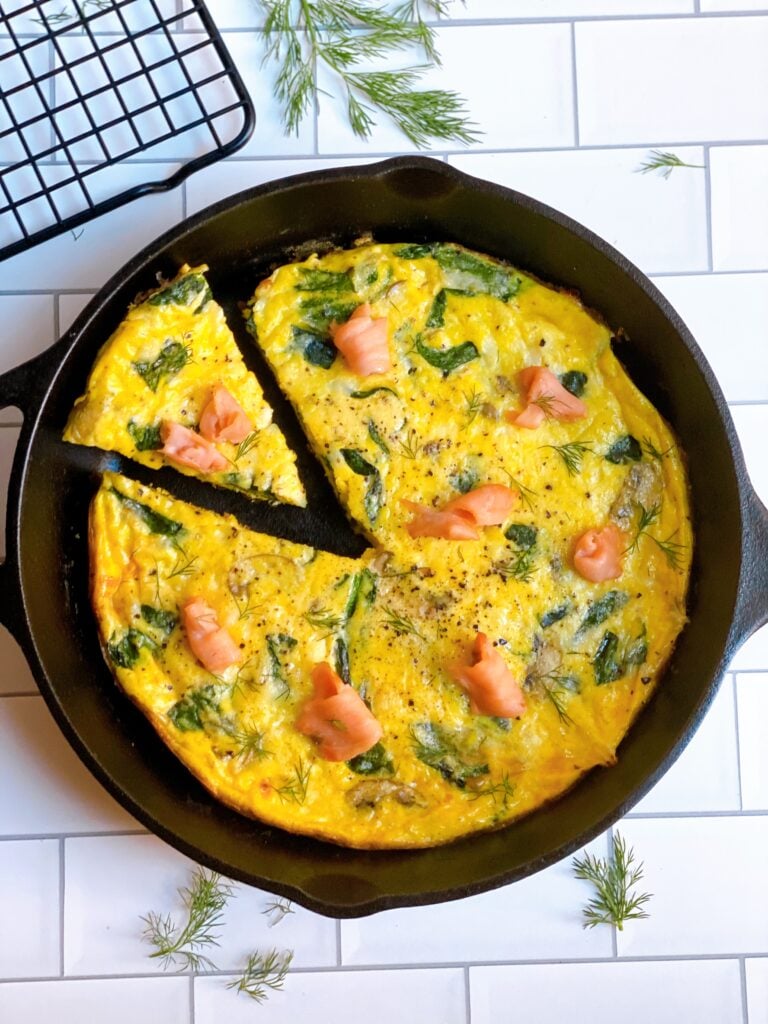 Spinach, Mushroom and Smoked Salmon Cheese Frittata in a skillet with one slice cut