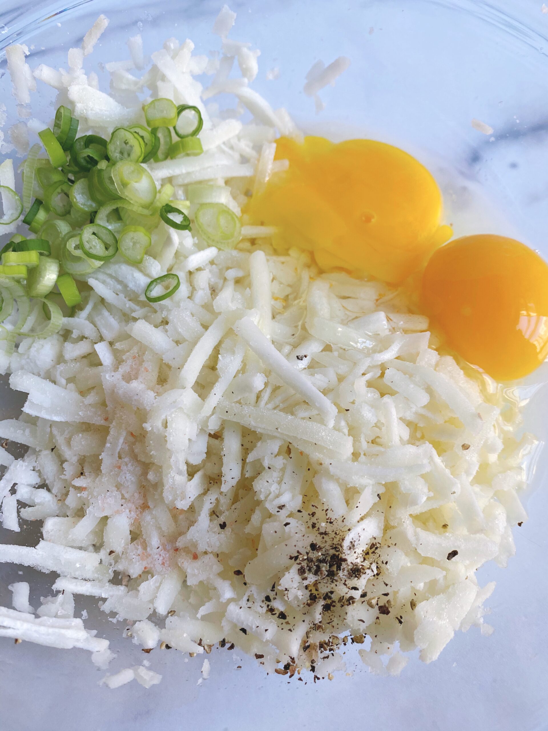 Close up of shredded frozen potatoes, two raw eggs and thinly sliced green onions in a bowl.