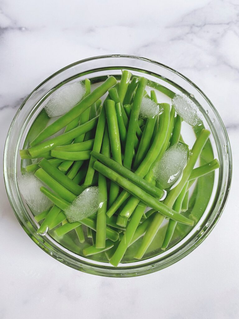 A bowl of green beans immersed in ice water; part of the blanching process.