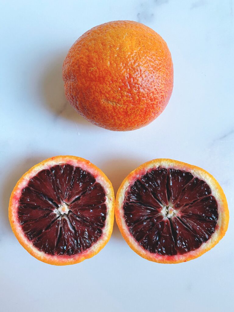 Overhead view of one whole blood orange and one blood orange sliced into two