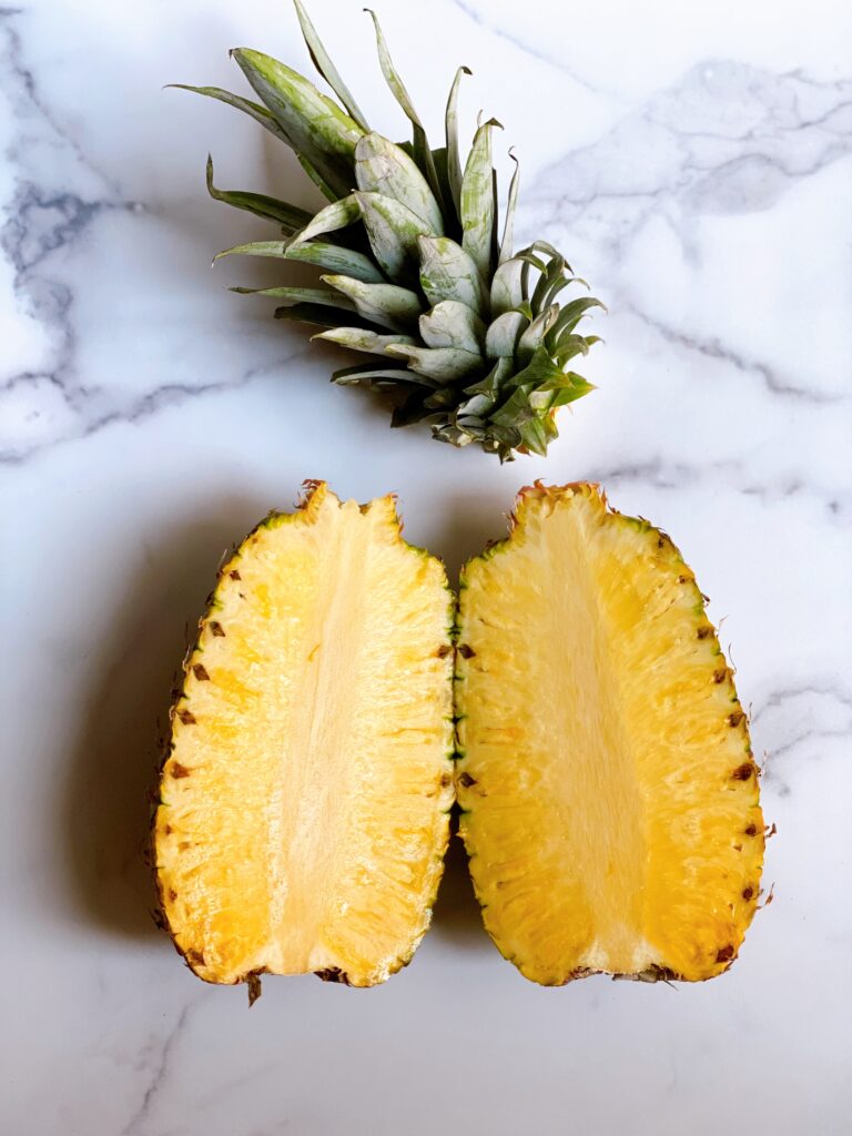A pineapple sliced in two with the stem removed.