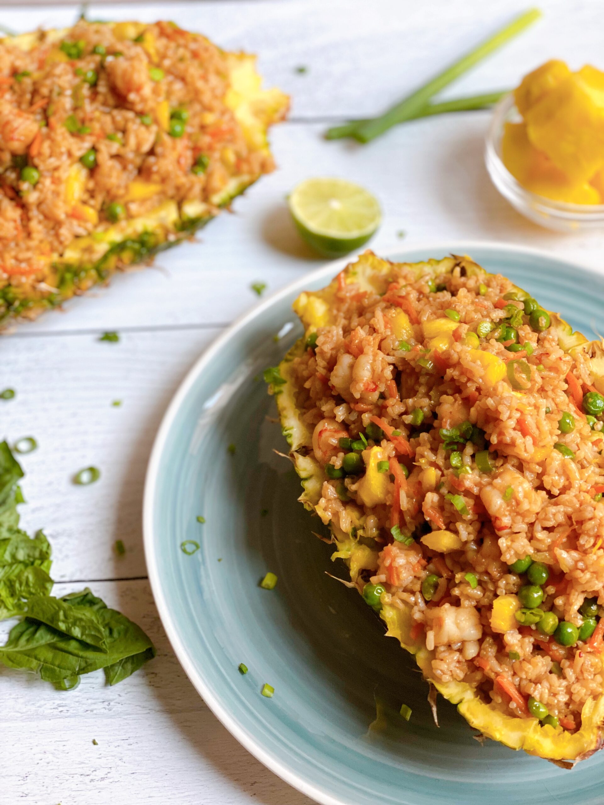 A pineapple filled with Pineapple Shrimp Fried Rice on a plate with another pineapple filled with rice in the background.