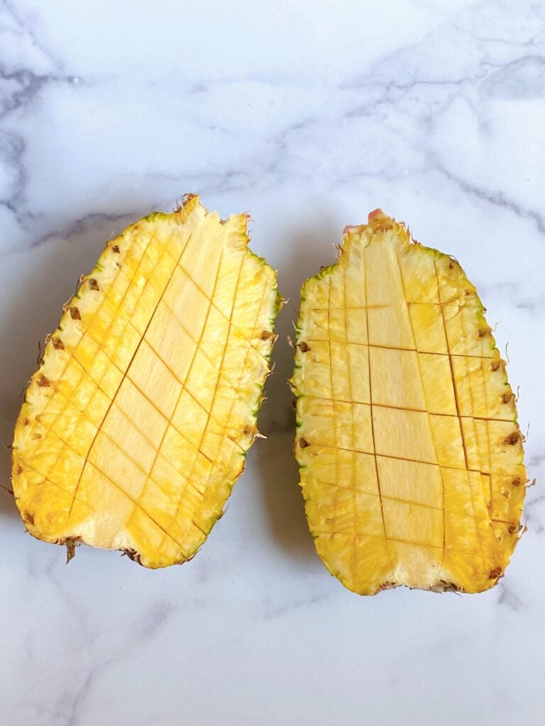 Two halves of a pineapple, sliced into squares