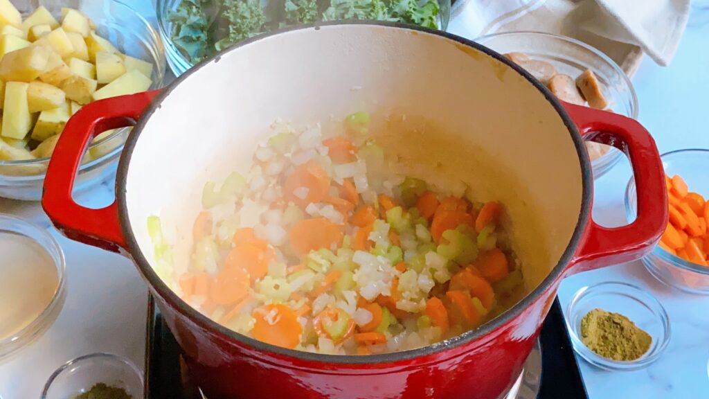 Overhead view of a red pot filled with onions, carrots, celery and garlic.