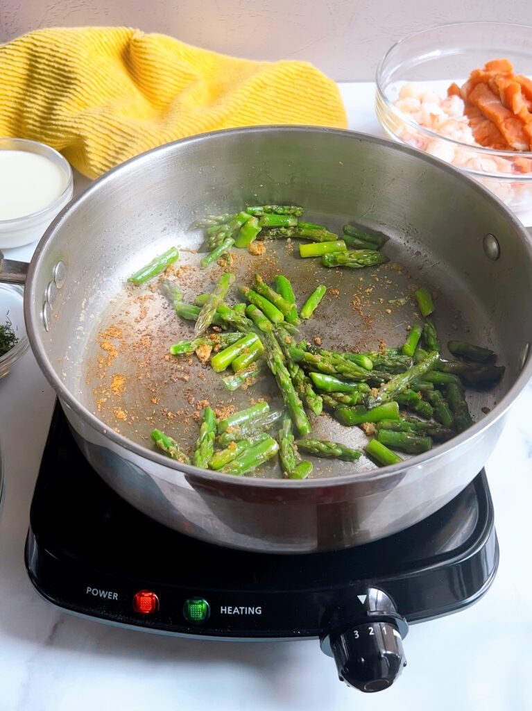 Asparagus being sautéed in a pan with butter and garlic powder
